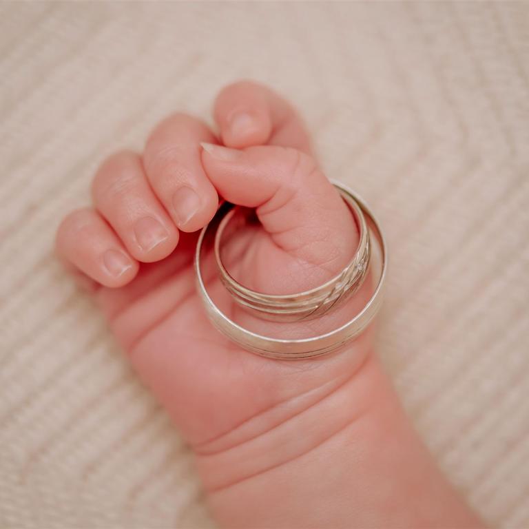 zarte Babyhand mit Mamas und Papas Ring in der Hand