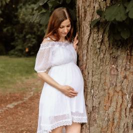 schwangere Frau lehnt am Baum und bewundert ihren Babybauch
